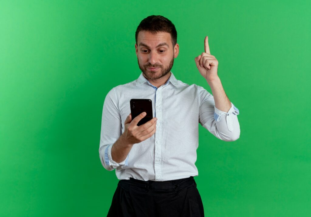 Uma pessoa segurando um smartphone e apontando para cima, em frente a um fundo verde.
