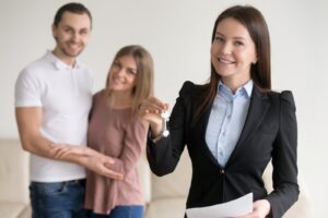 Corretor de imóveis, sob as categorias do CRECI, entregando chaves a um casal, representando uma transação imobiliária bem-sucedida.